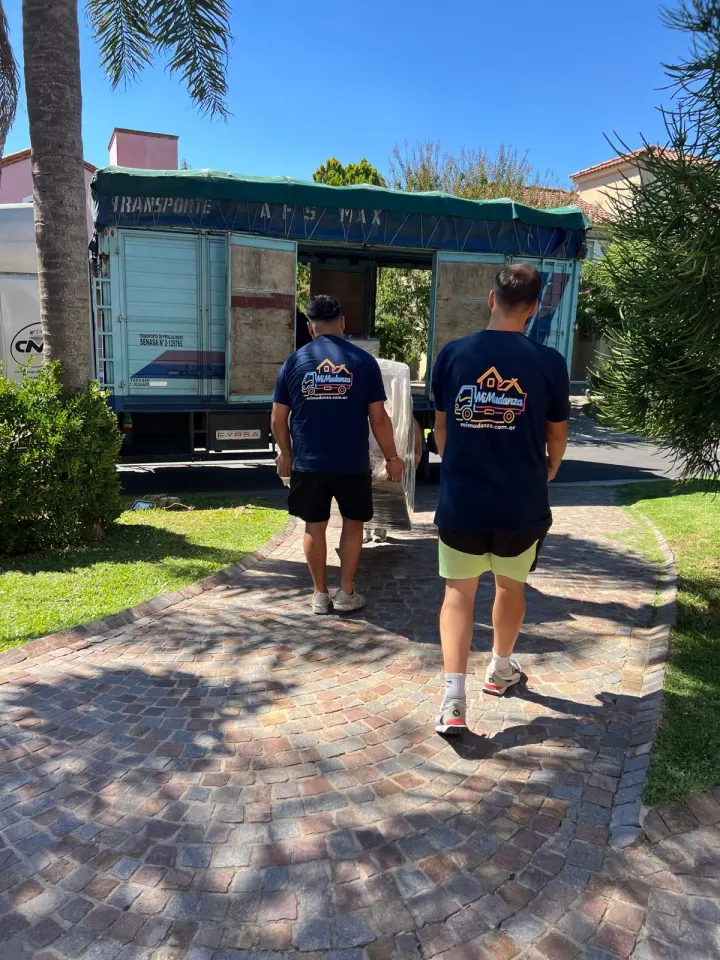Dos integrantes del equipo de Mi Mudanza caminando hacia el camión en una casa con jardín
